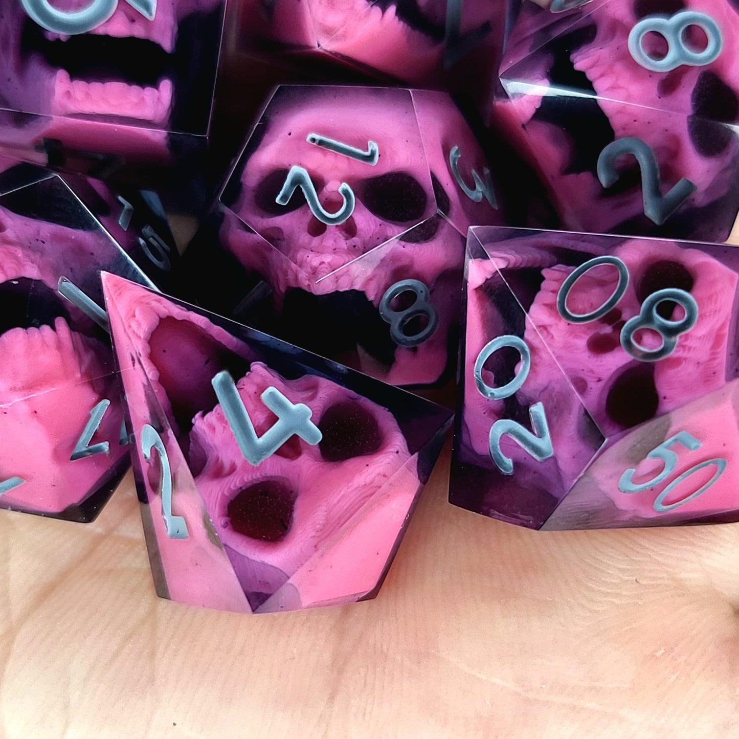 Close-up of black resin dice with pink undead zombie skulls and grey numbers, handcrafted by Mefisto_Dice.