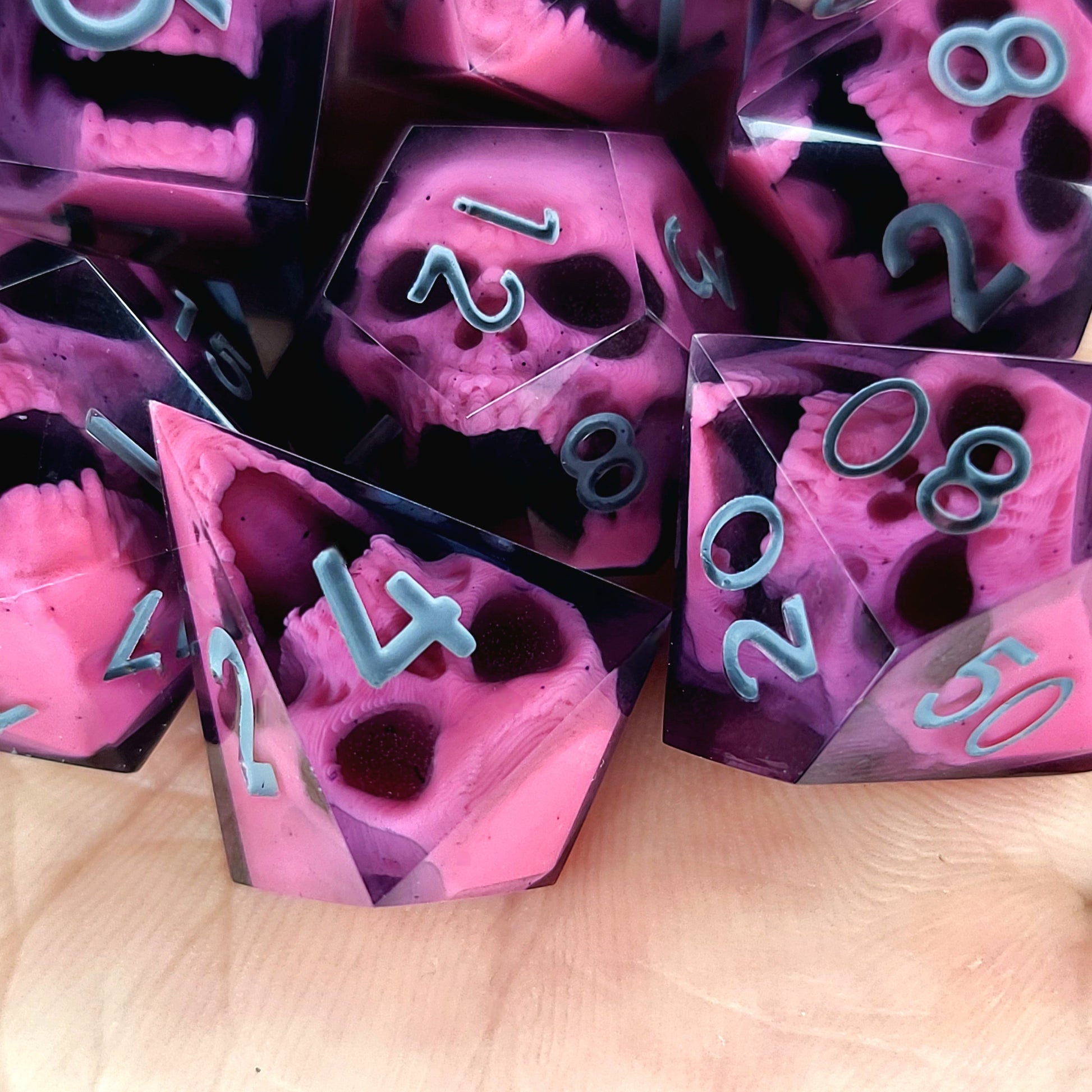 Close-up of black resin dice with pink undead zombie skulls and grey numbers, handcrafted by Mefisto_Dice.