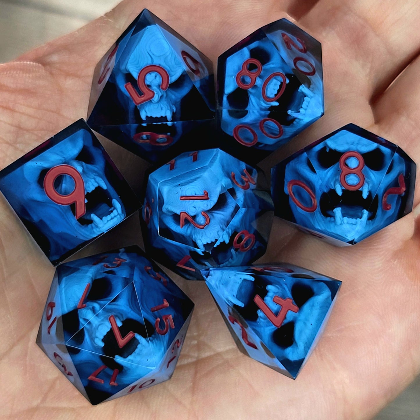 Blue resin DnD dice set with light blue skulls inside and red engraved numbers