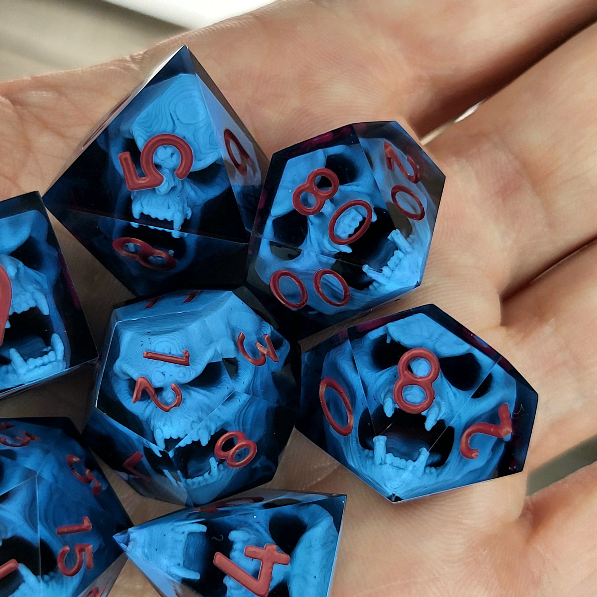 Blue resin DnD dice set with light blue skulls inside and red engraved numbers