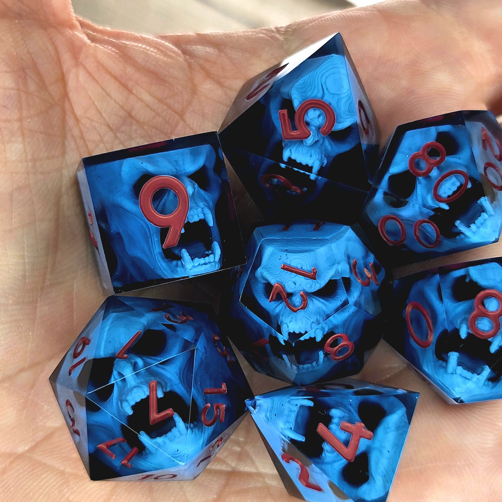 Blue resin DnD dice set with light blue skulls inside and red engraved numbers