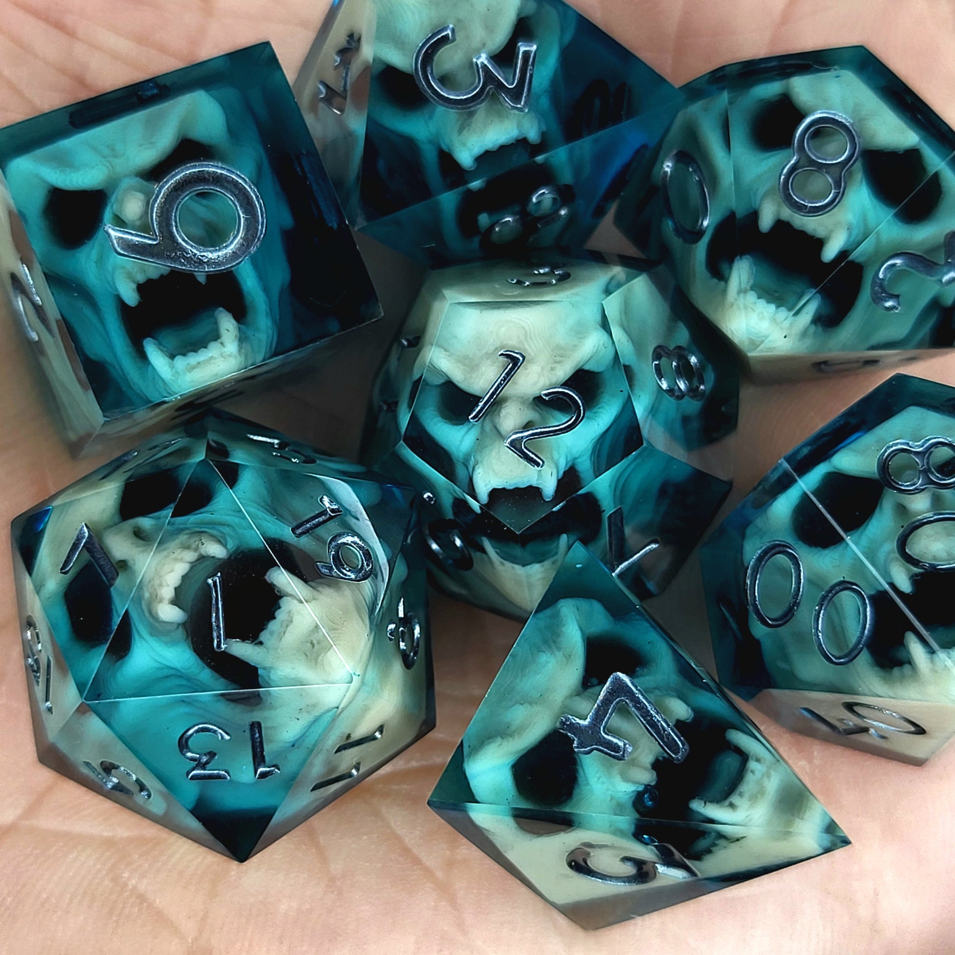 Teal and black resin DnD dice set with bone-colored skulls inside and metallic silver numbers