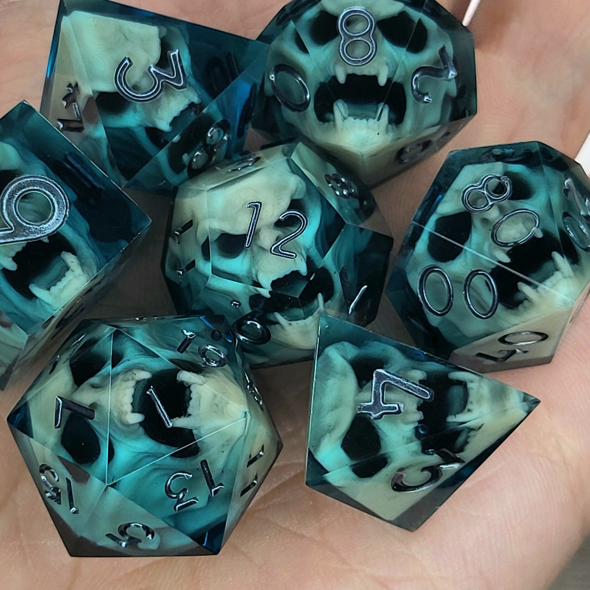 Teal and black resin DnD dice set with bone-colored skulls inside and metallic silver numbers