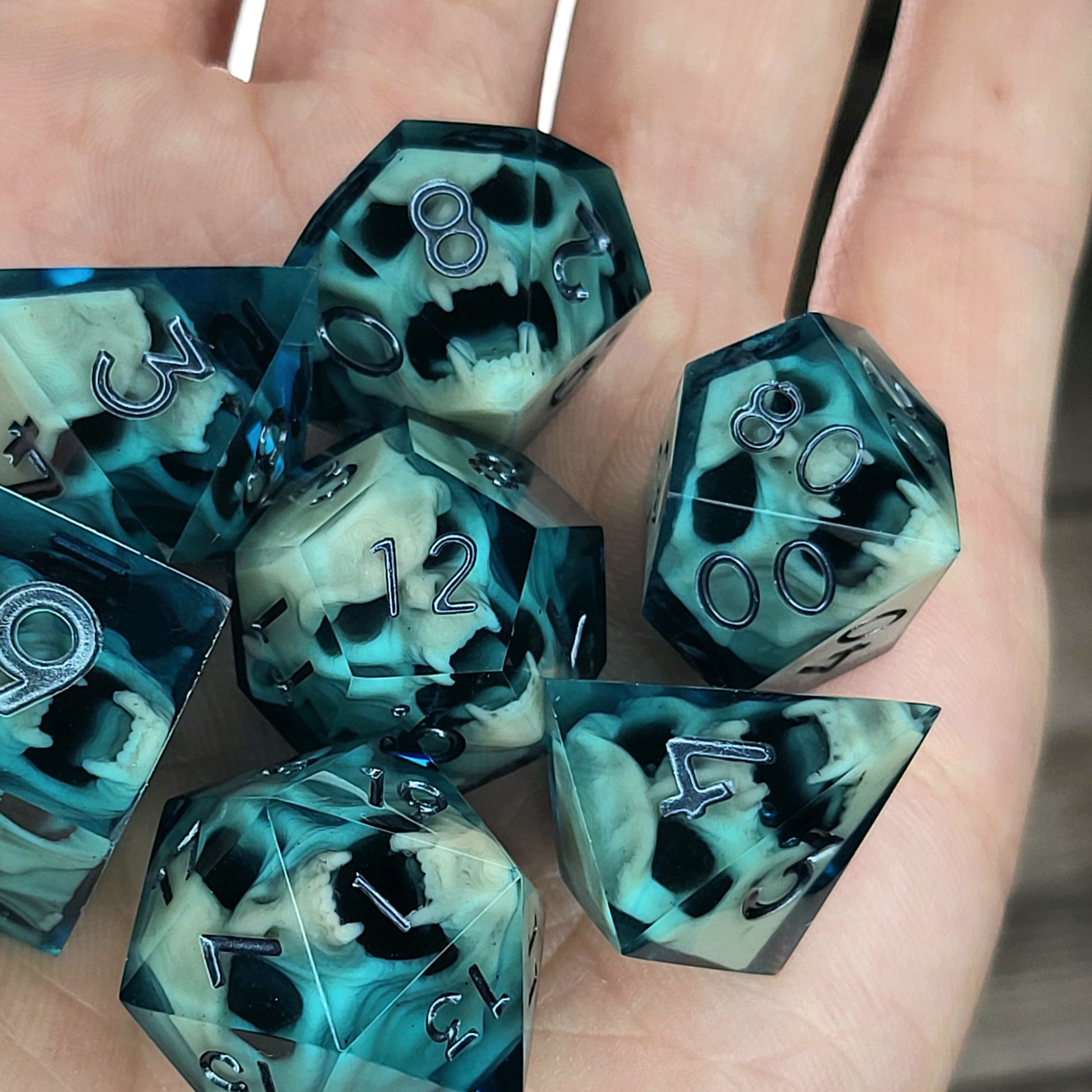 Teal and black resin DnD dice set with bone-colored skulls inside and metallic silver numbers
