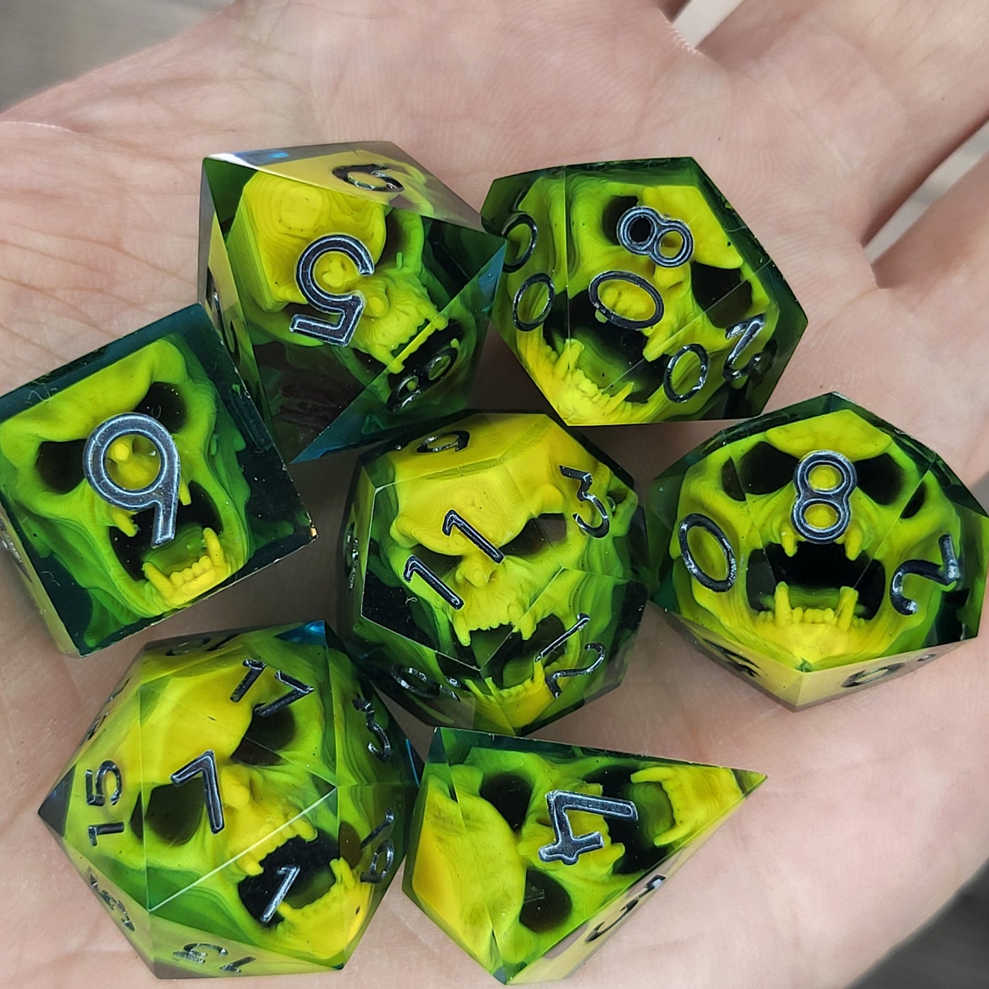 Blue resin DnD dice set with bright yellow skulls inside and silver engraved numbers