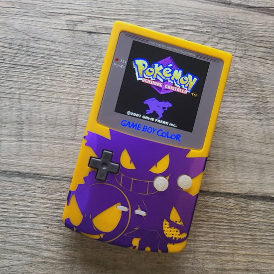 A customized Nintendo Gameboy color with yellow and purple Gengar pokemon on the front cover and backlit display