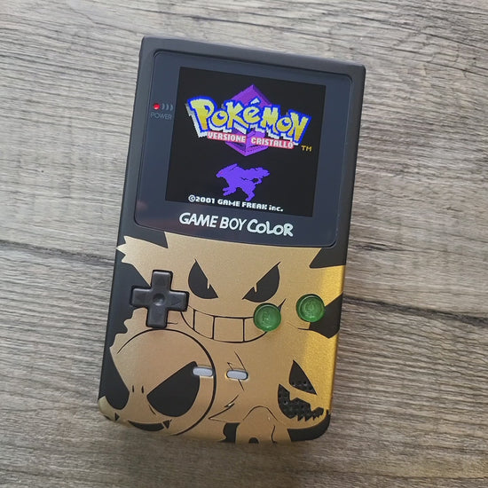 A customized Nintendo Gameboy color with black and gold Gengar pokemon on the front cover