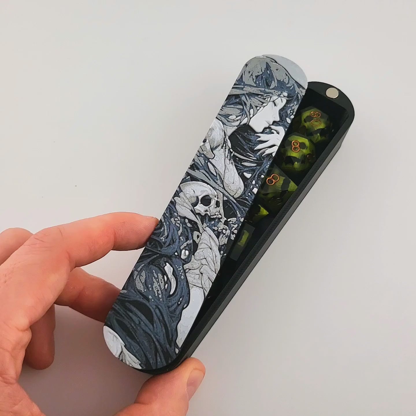 Close-up of a dice box featuring a detailed dark fantasy illustration of a woman surrounded by swirling shadows and skull motifs, shown partially open with RPG dice stored inside, designed by Mefisto_Dice.